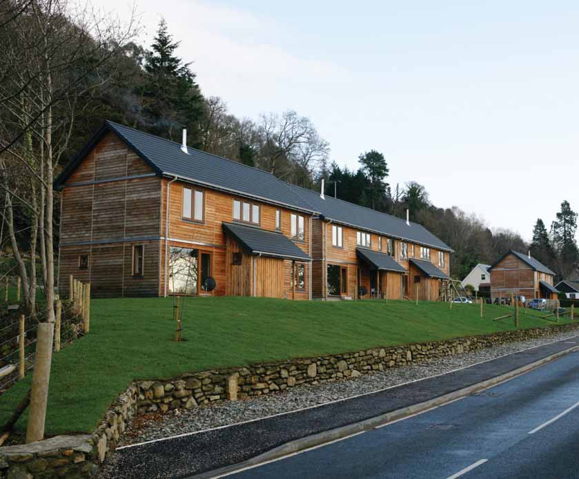 Three semi-detached houses in Kilmun, positioned on a slope beside the main road, with horizontal timber cladding facades. 