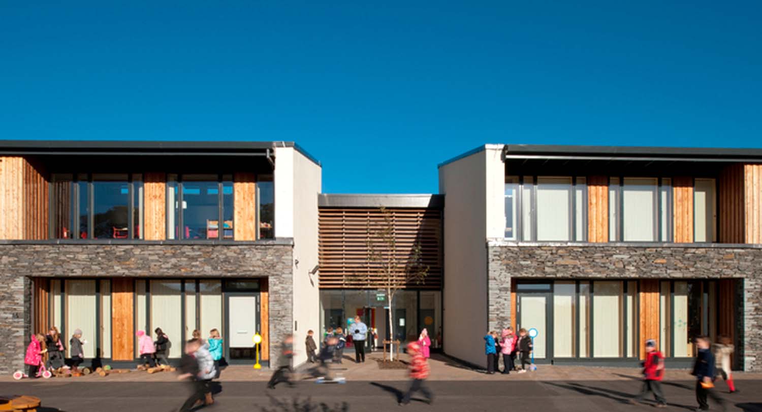 Exterior view of a school's classrooms. They have floor-to-ceiling windows and are connected by a corridor.