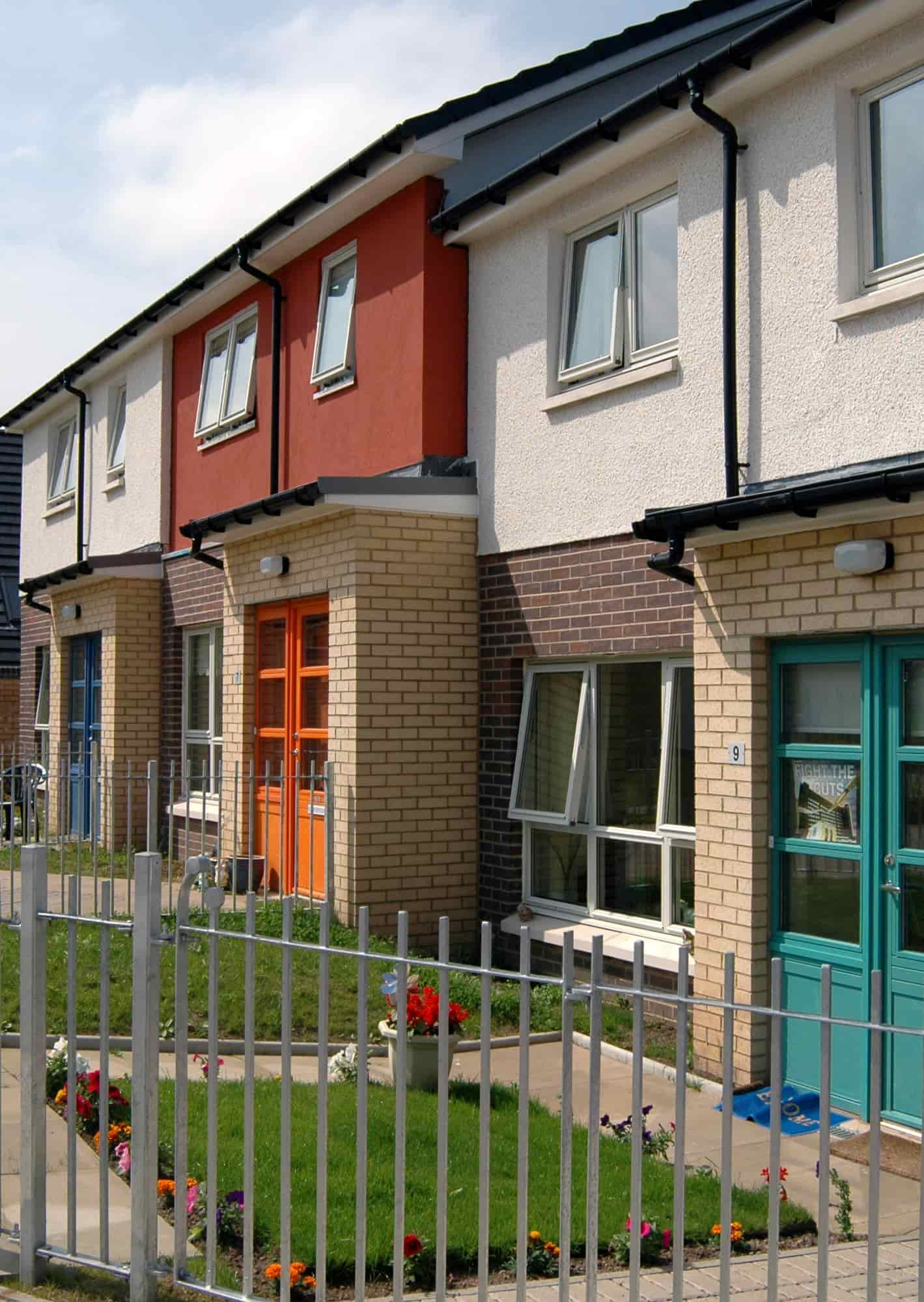 A close up of a row of two-storey houses with colourful front doors on a sunny day.