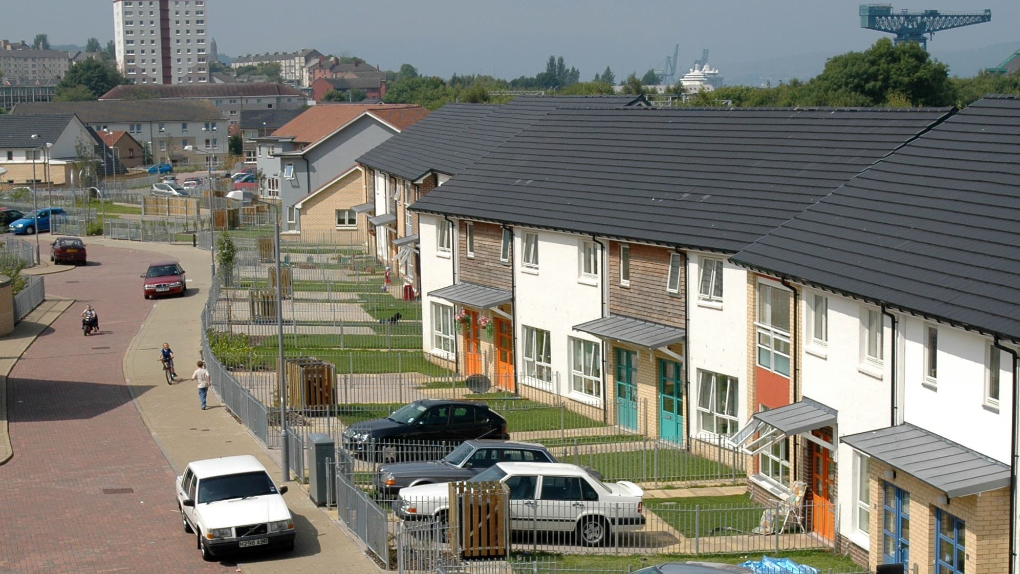 A row of two-storey houses with front gardens overlooking a quiet street.