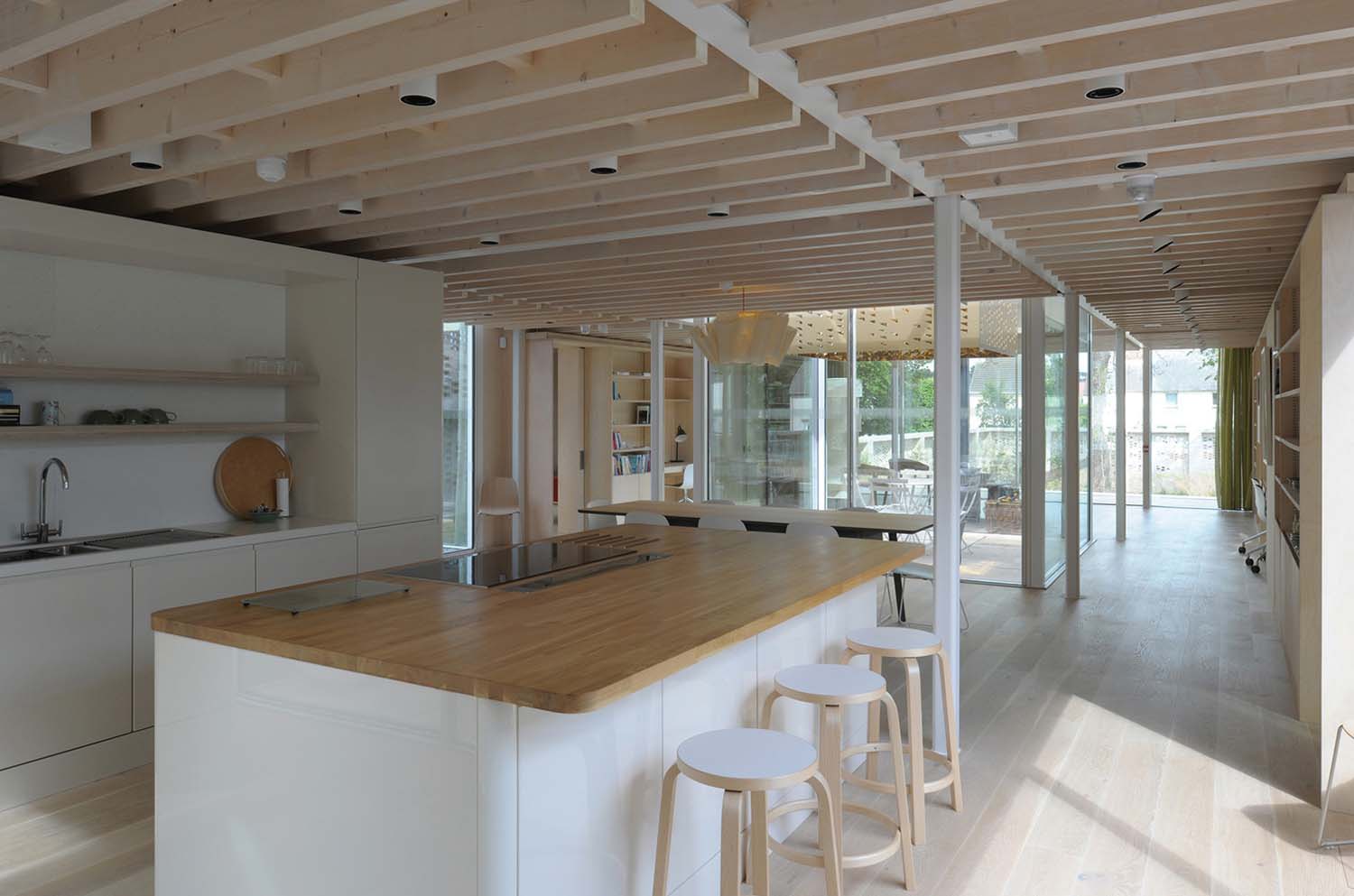 An interior shot of a kitchen and social area with light coloured wood and a large window at the back of the building