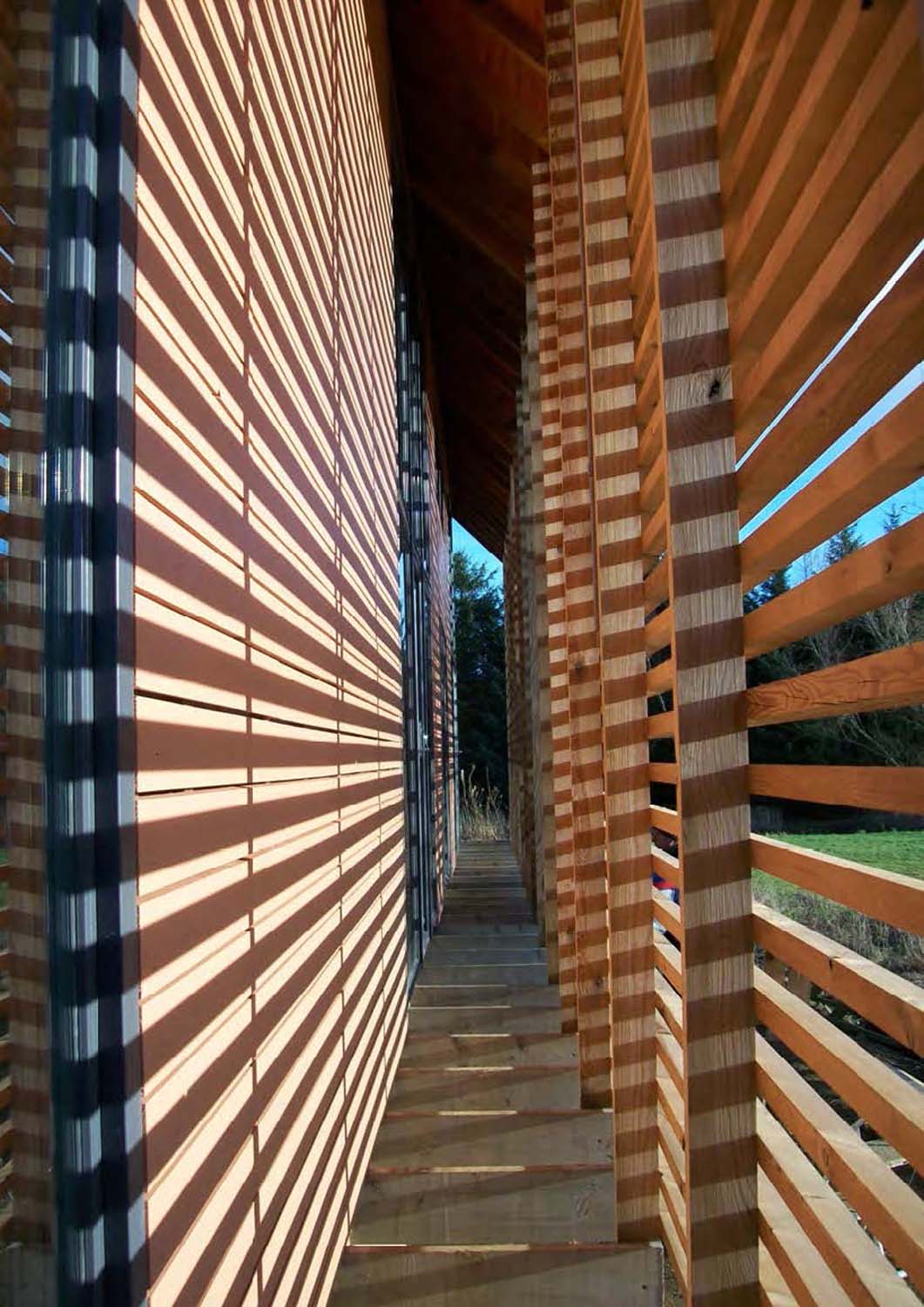 A photograph between two sections of external wall made from timber - one provides a screen and one is a solid wall