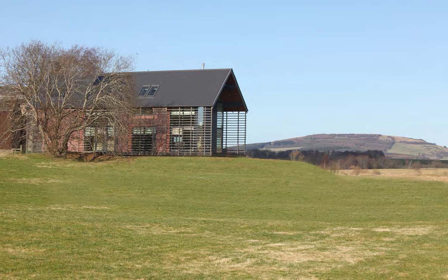 A photograph of  large timber building sitting on a small hill in an open landscape