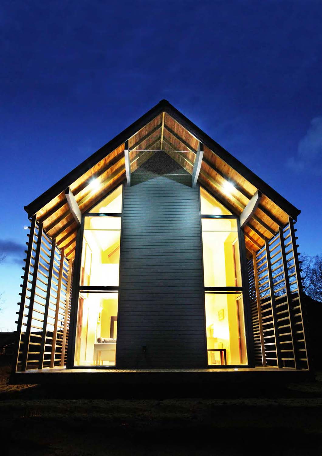 An exterior photograph of a two-storey house at night time with the internal lights on against a dark blue sky