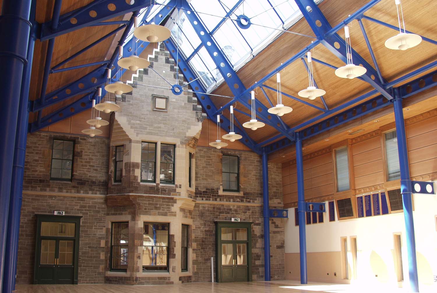 A photograph of an interior courtyard with the view of an old stone building in the background and blue columns supporting a glass roof