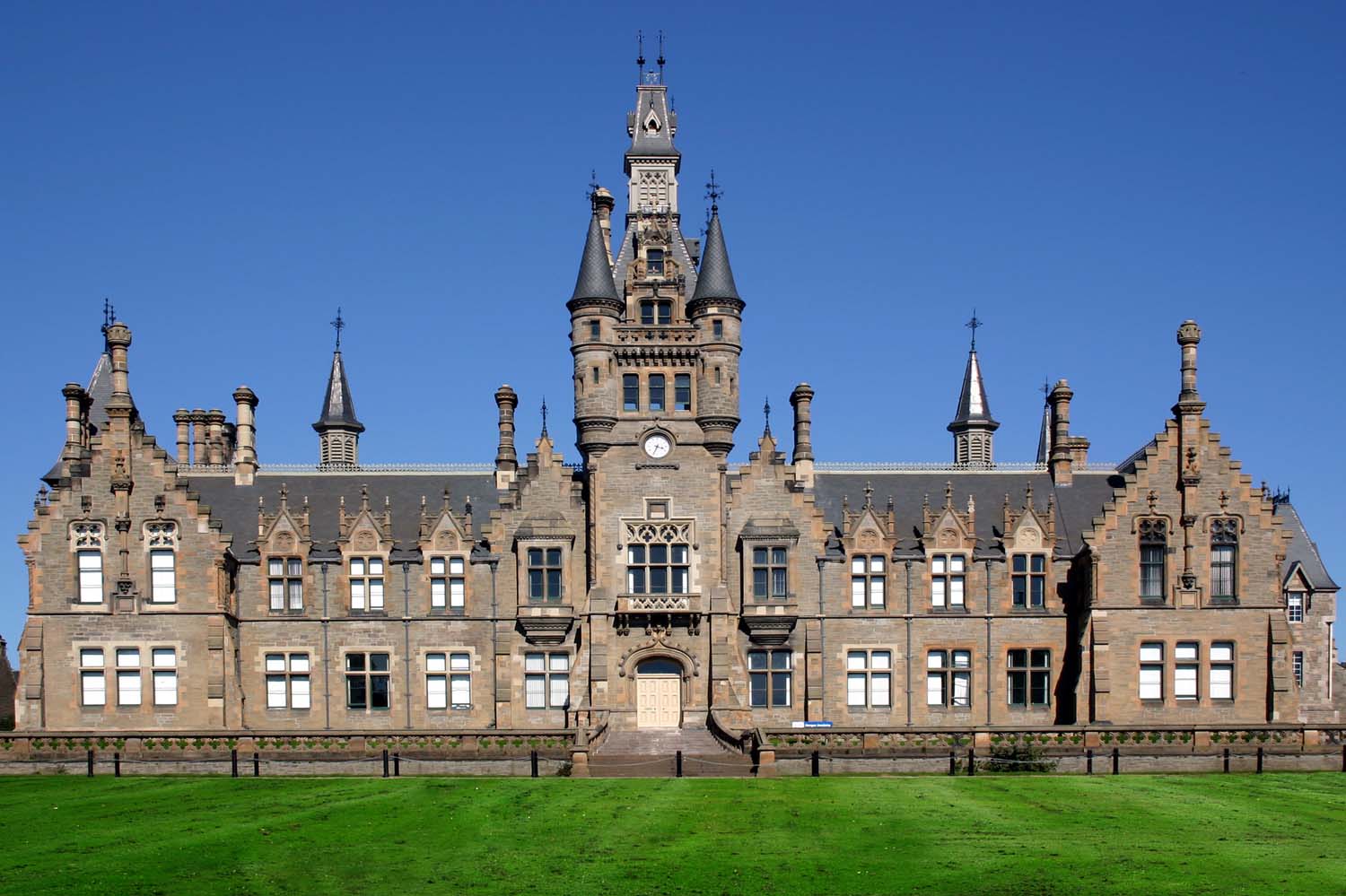 The exterior view of a large victorian school building built from site and with a large clock tower at the centre of the image