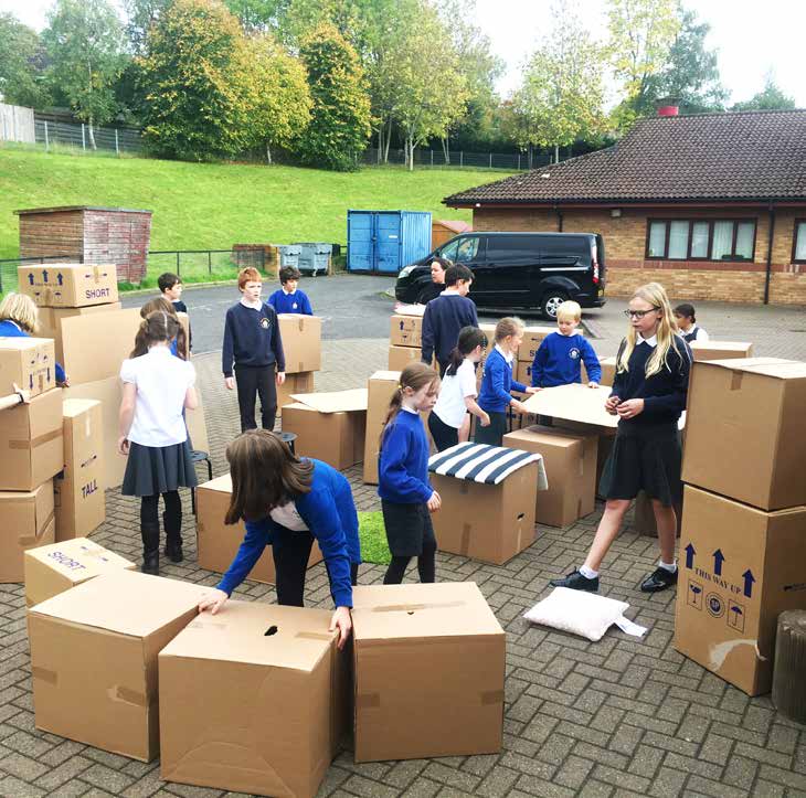 A group of pupils test their design ideas in a parking space during a Tests of Change workshop by building a classroom from cardboard boxes.