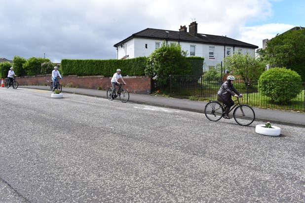A group of people cycling down a street with a makeshift cycle lane marked out by tyres painted white.