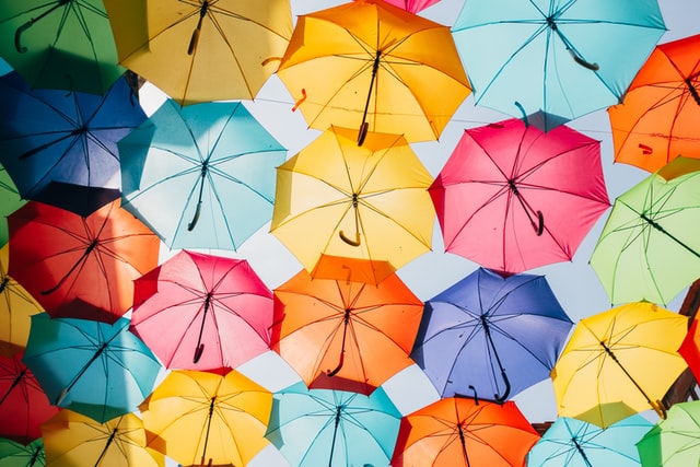 A view from the ground to a canopy of rainbow coloured umbrellas against a blue sky