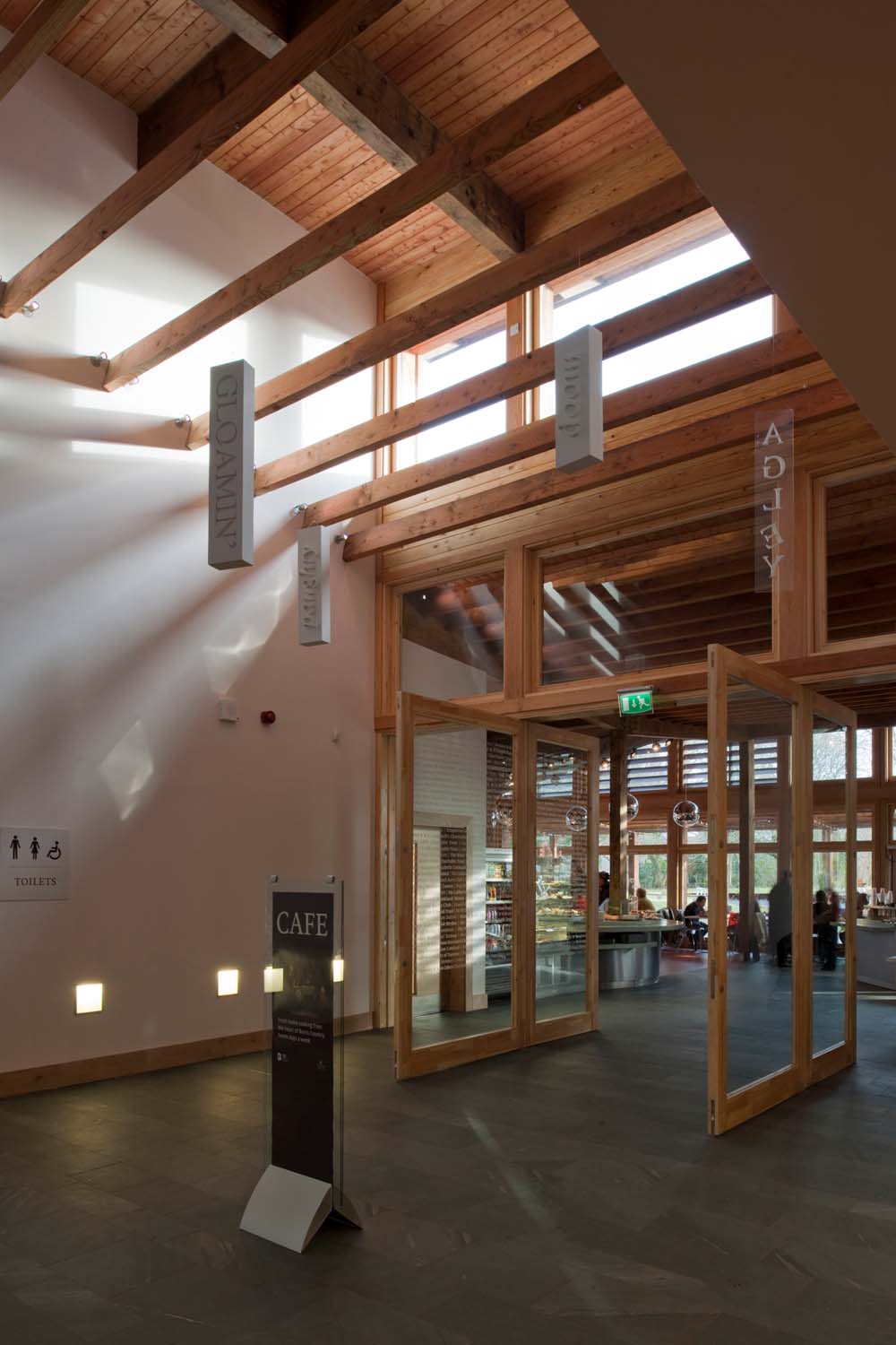 The indoor cafe entrance to Robert Burns Birthplace Museum. It has a double-height space area with timber beams and signs hanging below them.