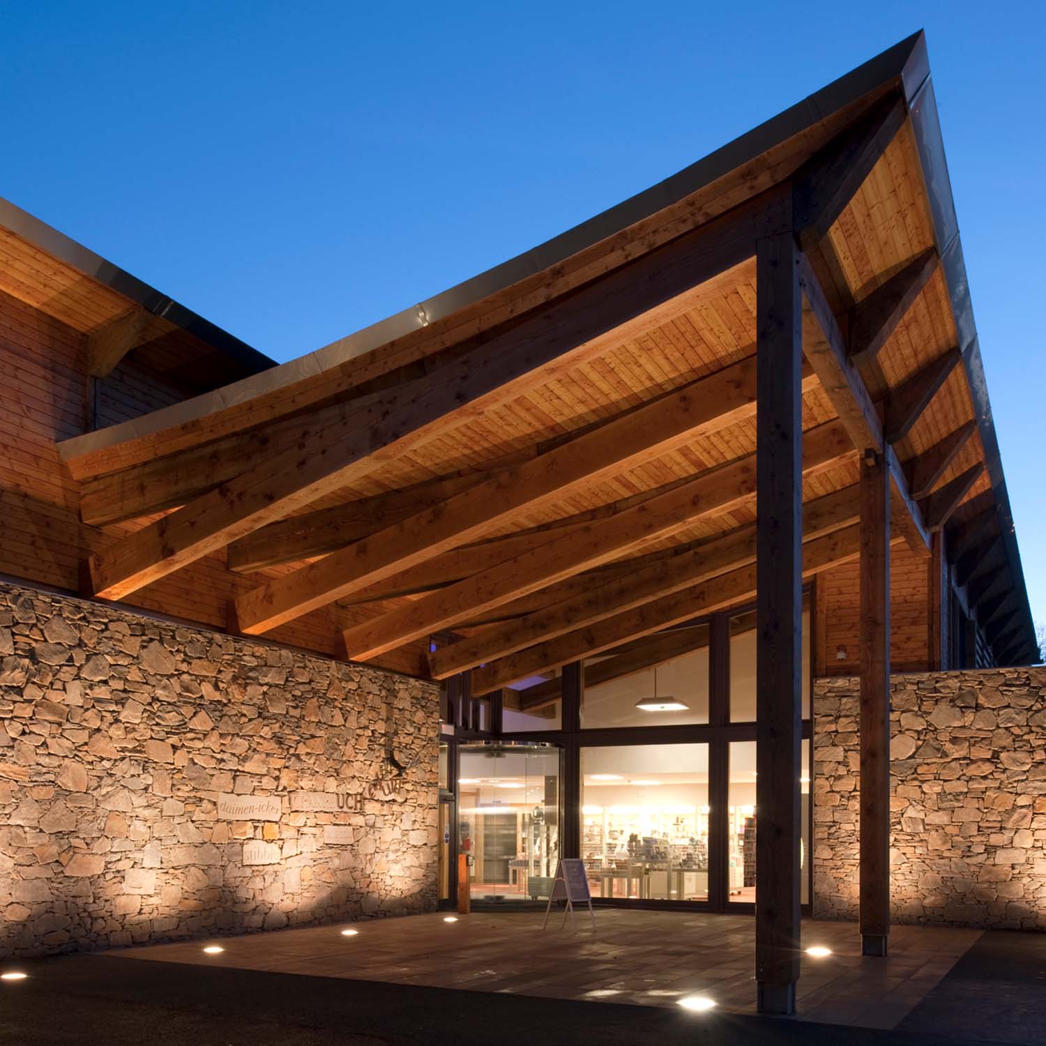 An exterior view of Robert Burns Birthplace Museum's entrance in the evening. The entrance patio is covered with a large curved timber canopy