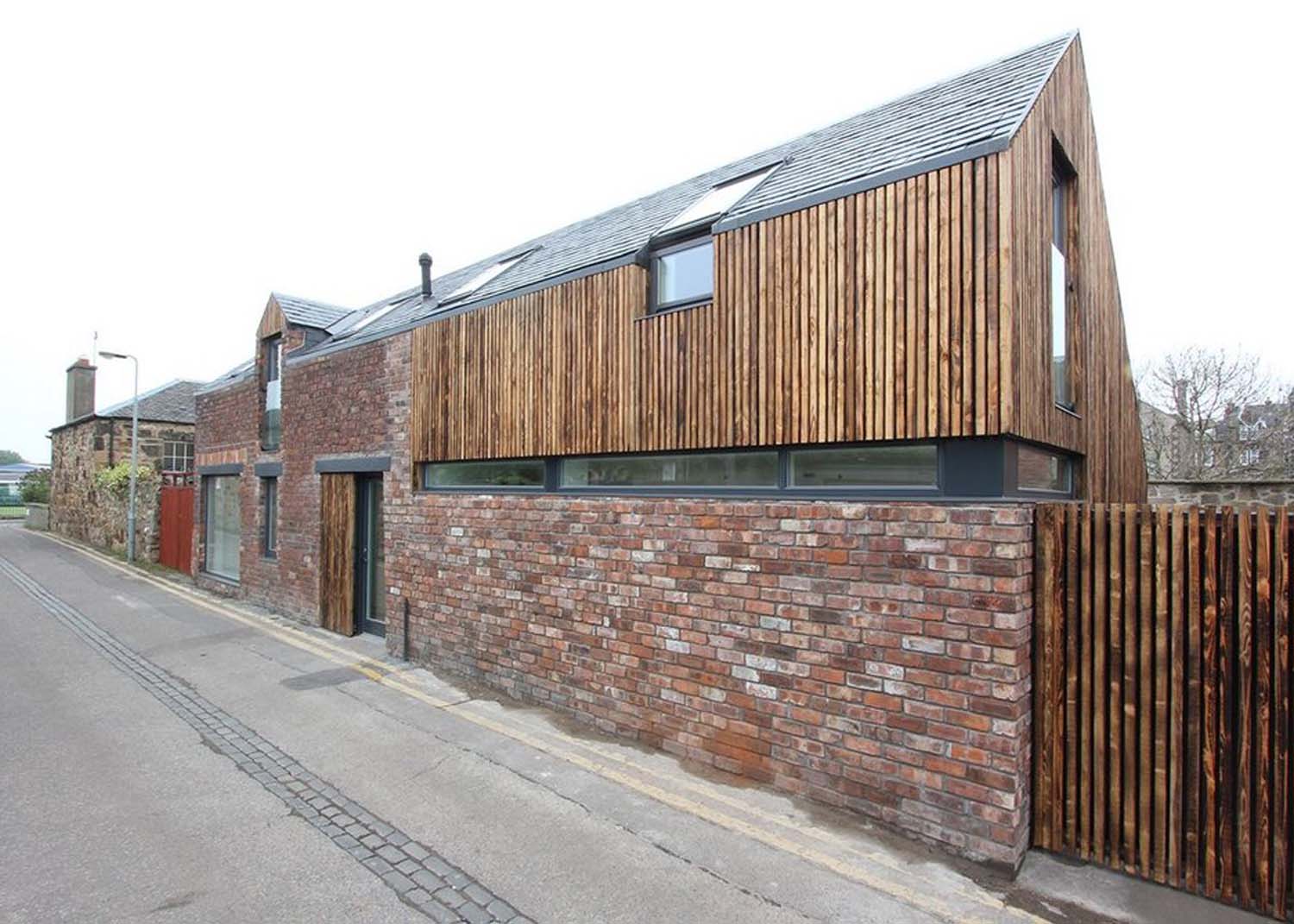 A street view of a house on Rosefield Avenue Lane with a ground floor red brick facade. Vertical timber slats cover the first floor and garage doors.
