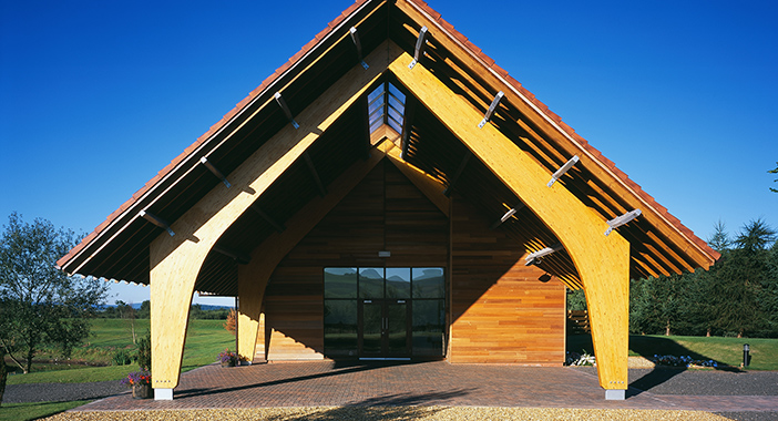 A crematorium building with low hanging roof. The building has a slight yellow patina to the wood.