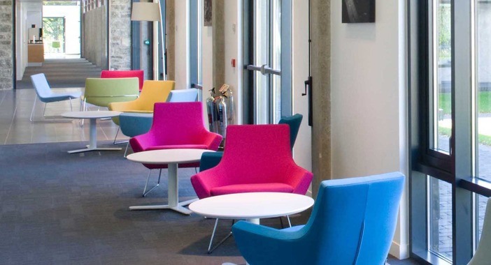 Break-out office space at Scotstoun House with rows of brightly coloured pink, blue, yellow and green chairs and low white tables placed opposite the window.