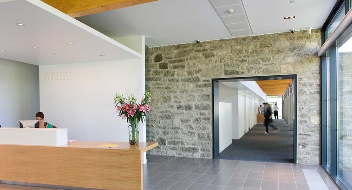 Light coloured stone wall behind the reception desk at Scotstoun House with a large black frame doorway leading to the office spaces.