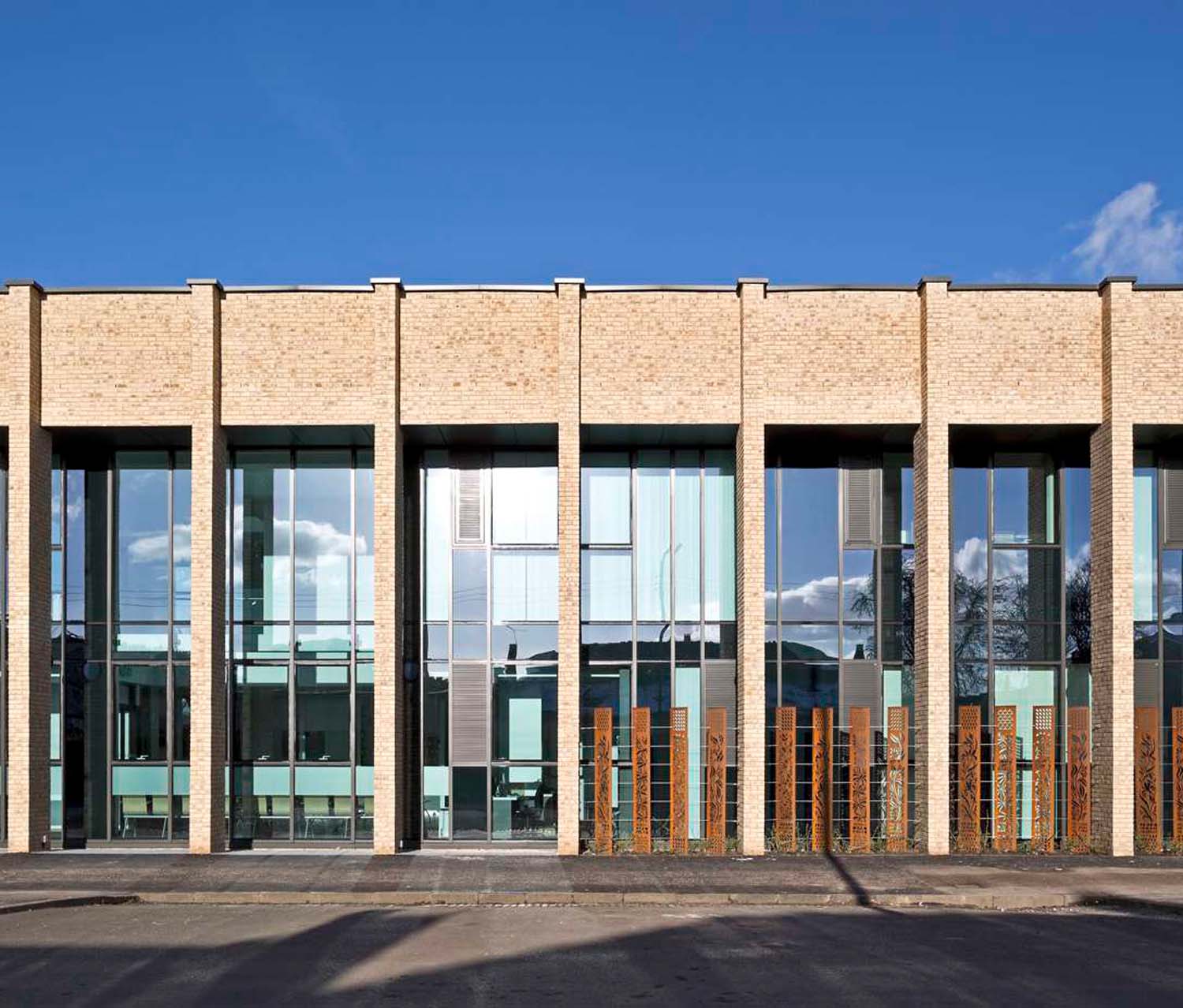 An exterior image of a buff coloured brick building with large windows and rust coloured screens on the right hand side of the image