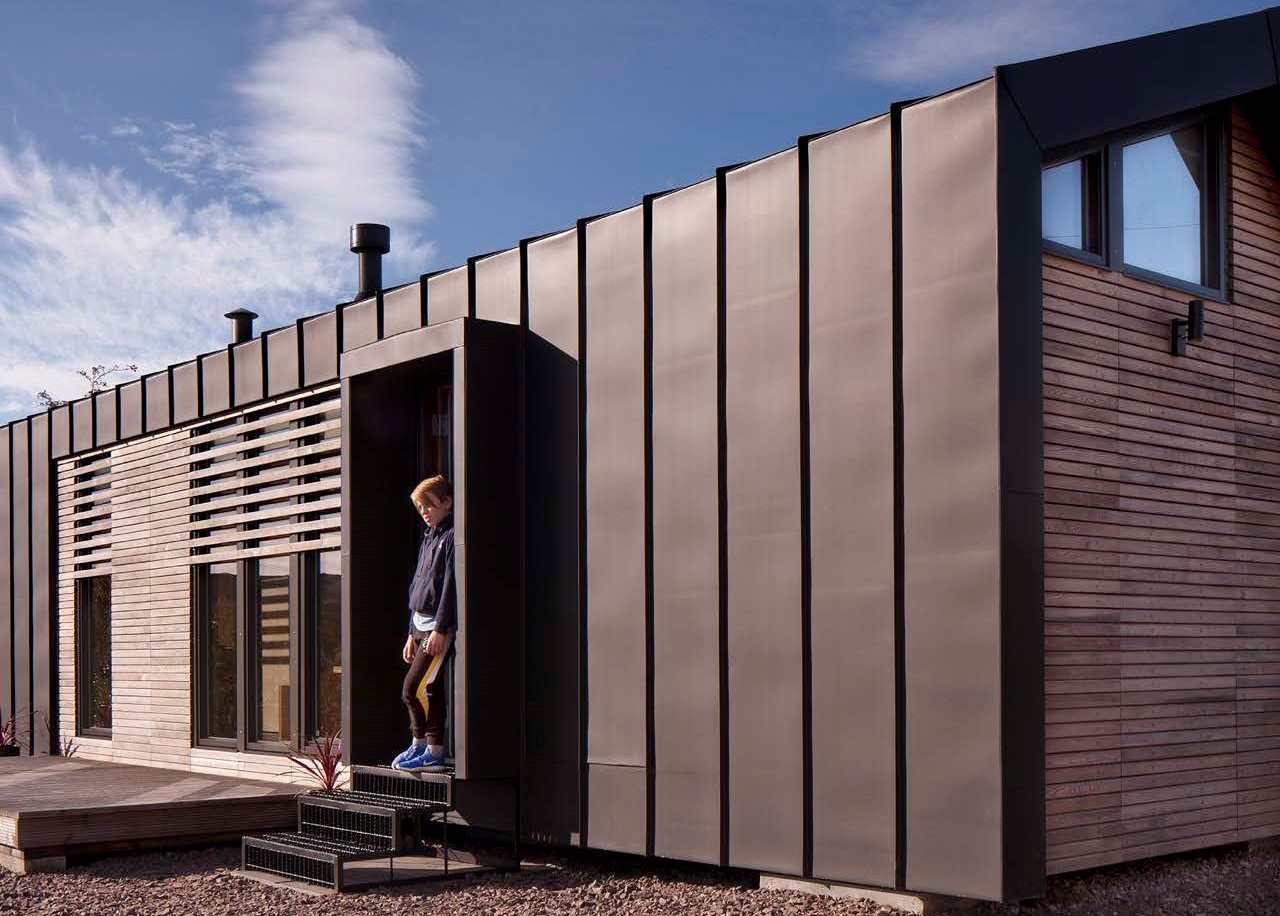 A boy standing at the entrance of the Skye Mobile Micro Home. The exterior walls are black metal cladding.