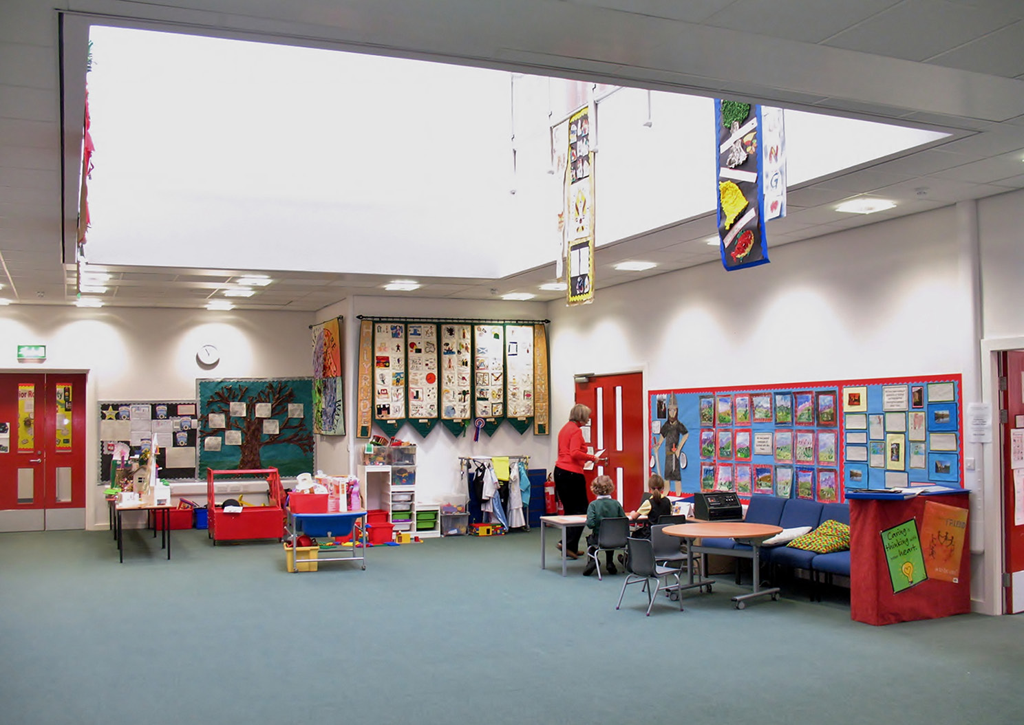 A learning area in Holyrude Roman Catholic Primary on the ground floor atrium space. There are two pupils and a teacher using the space.