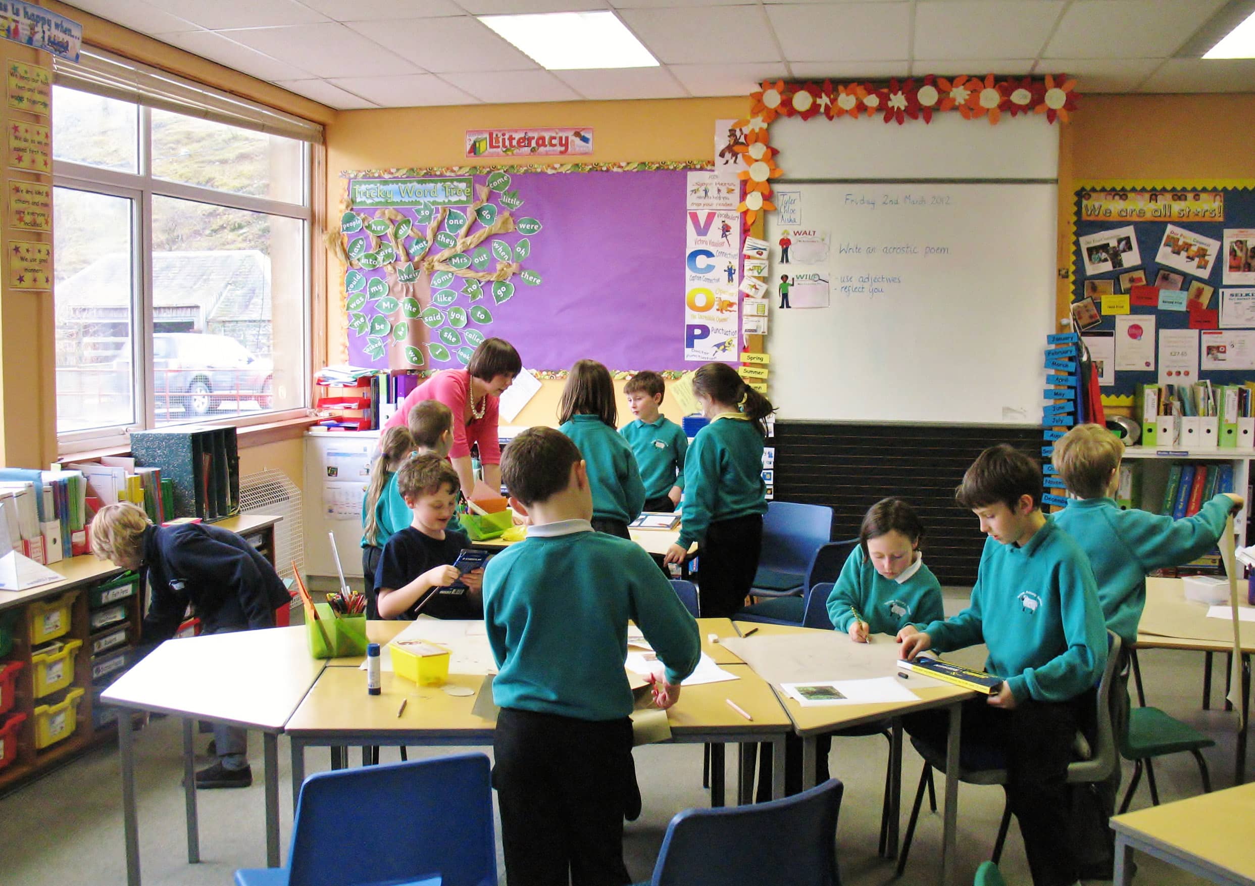 Children learn in a brightly coloured classroom at Yarrow Primary. The children are wearing teal coloured school uniform jumpers.