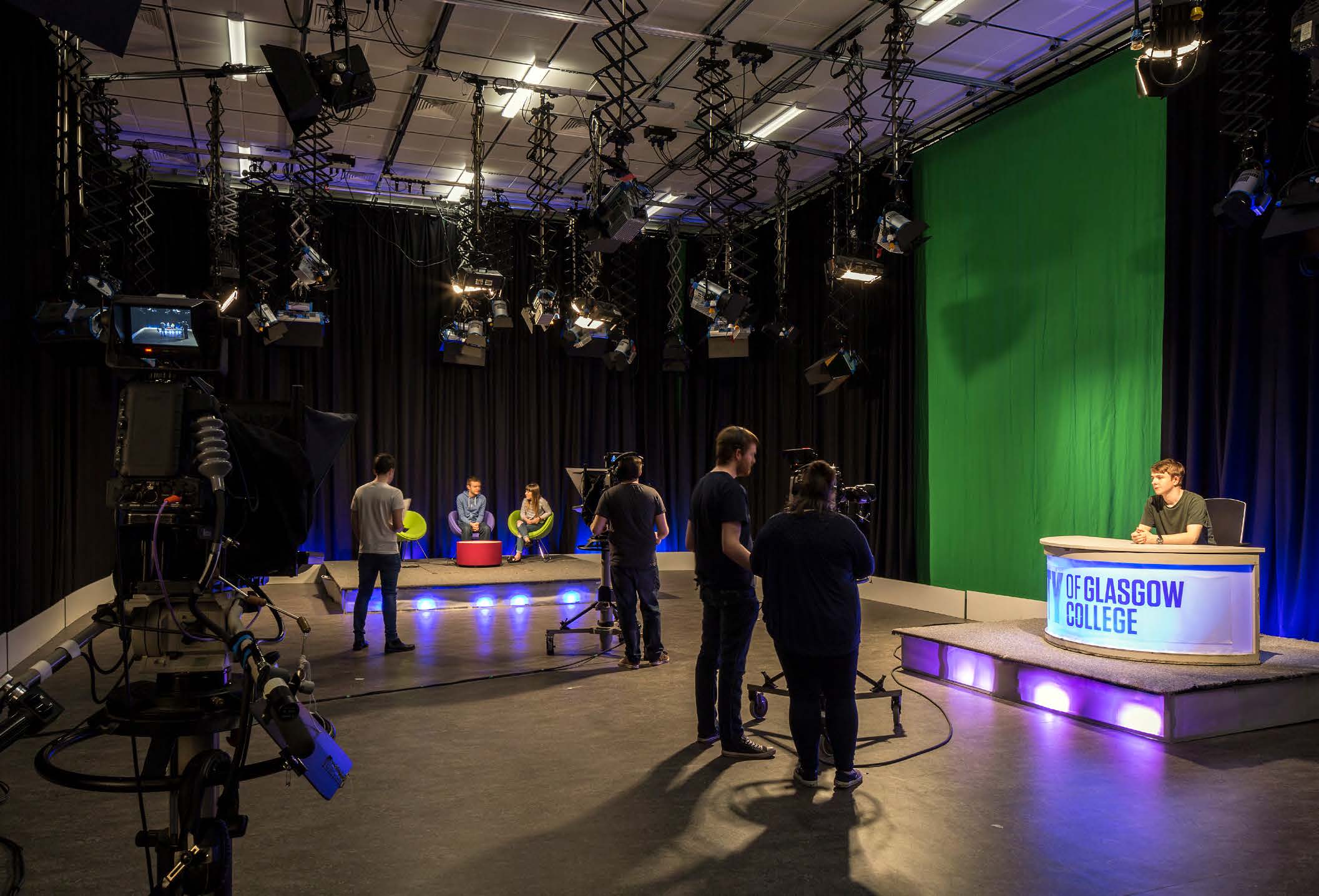 Students using a broadcasting teaching facility at City of Glasgow College. Black out curtains line the room with a green screen on the right wall.