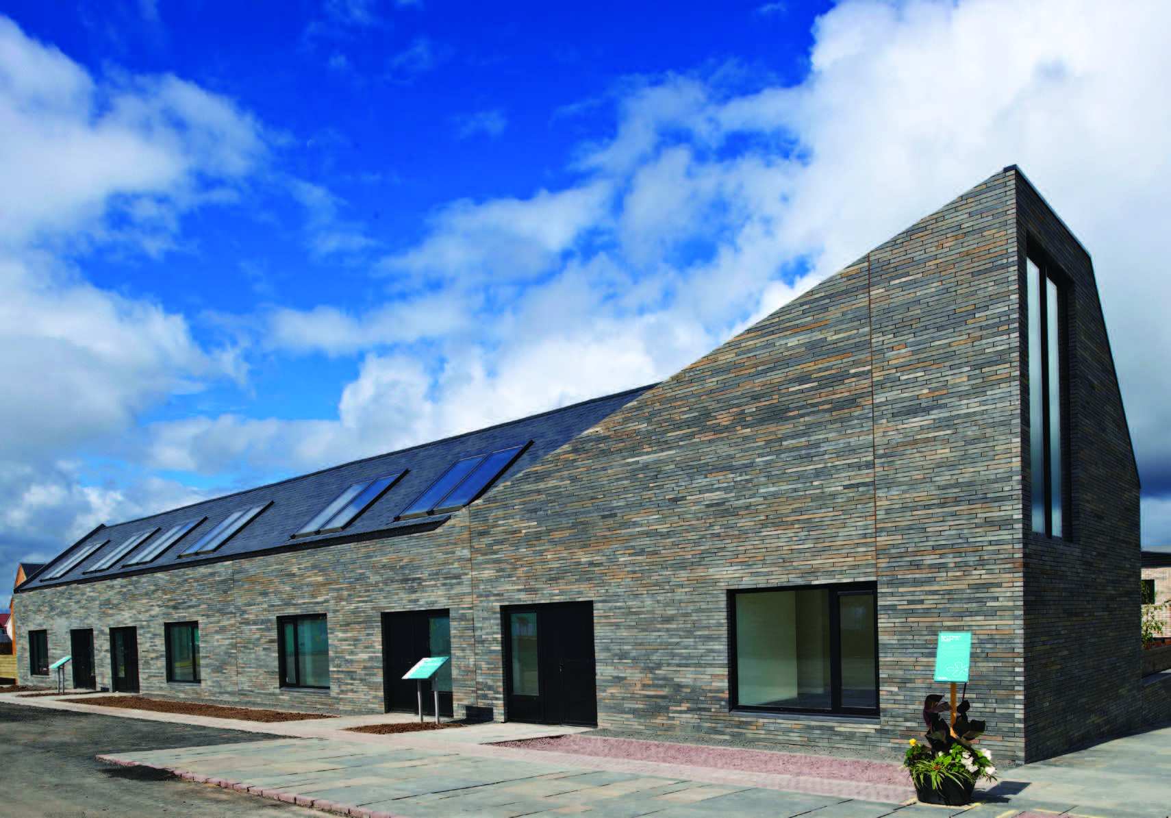 A row of attached houses with stone façade on a cloudy yet bright day. The entire building has a black stone roof with roof lights.