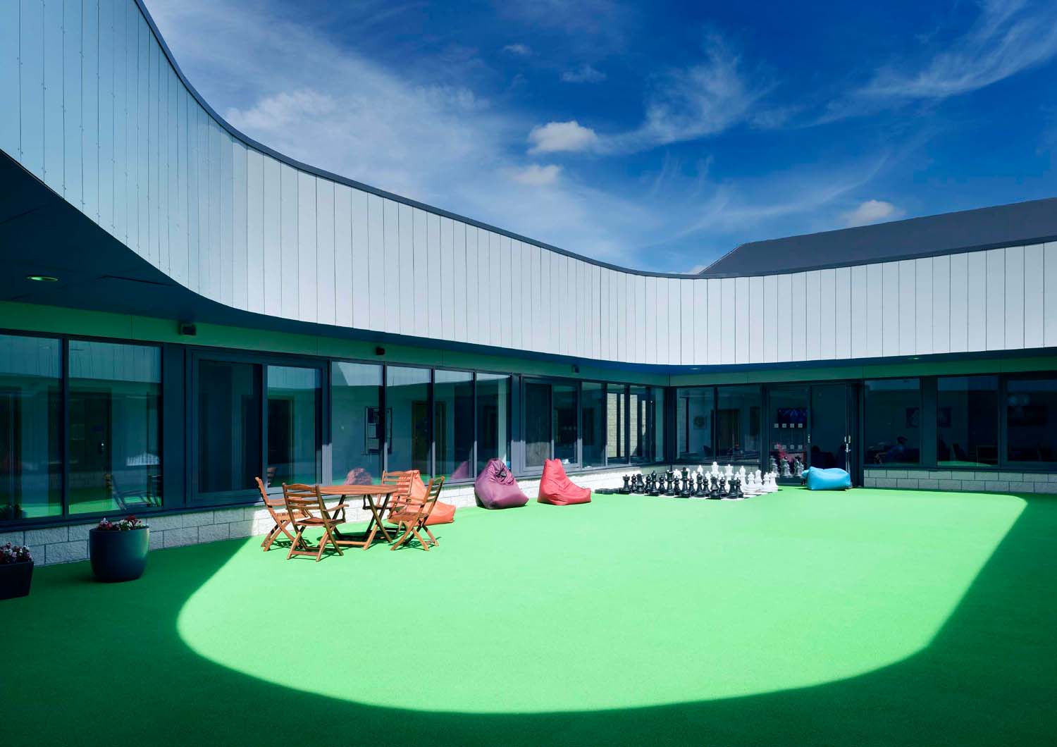 An internal courtyard with a green floor, chairs, bean bags and a giant outdoor chess set. The courtyard is surrounded by a glass wall.