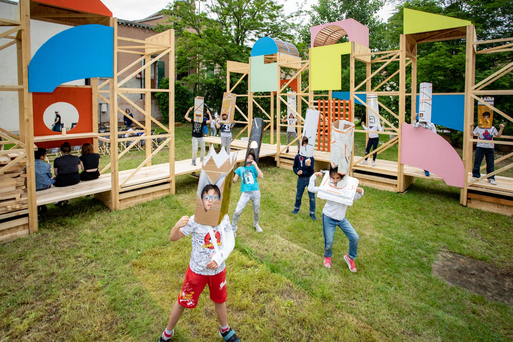 10 children are parading decorated, cardboard tower structures on their heads in The Happenstance’s garden venue.