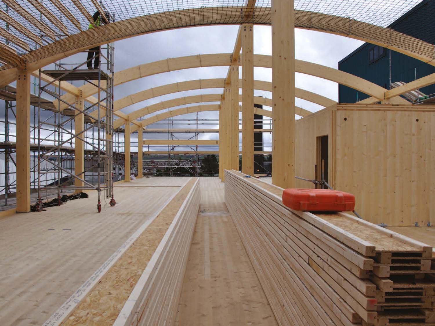 A builder working on the curved roof at Thurso College during its construction. There are long planks of wood in the centre of the space.