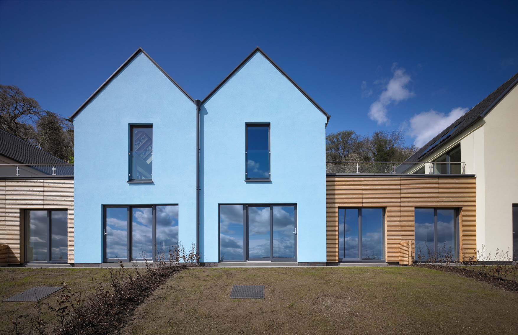 Two blue coloured attached houses and a garden leading up to the sliding doors.