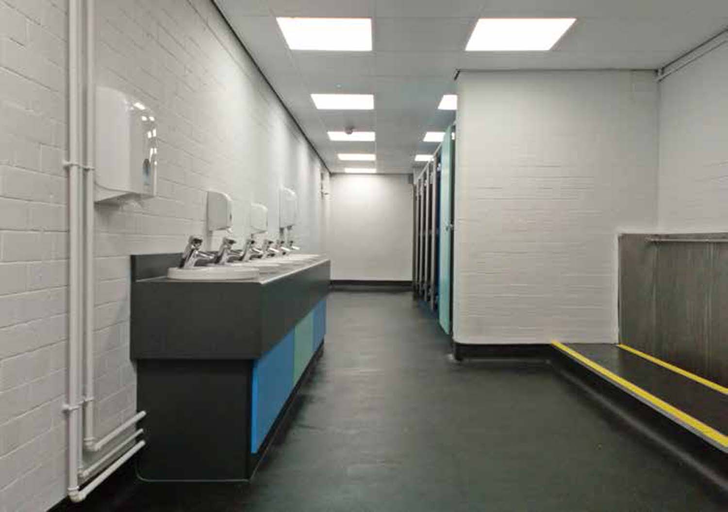 A corridor with a row of sinks on one side and a row of cubicles on the other.