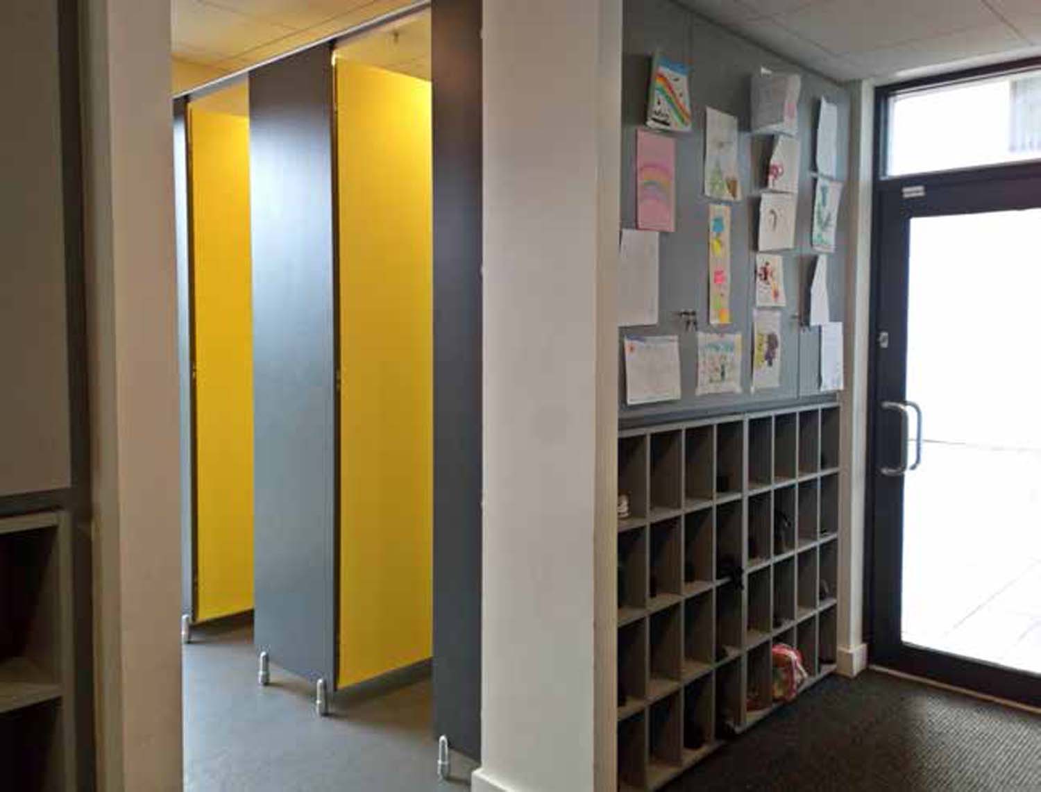 Toilet facilities with yellow cubicles next to shoes storage space and a building entrance.