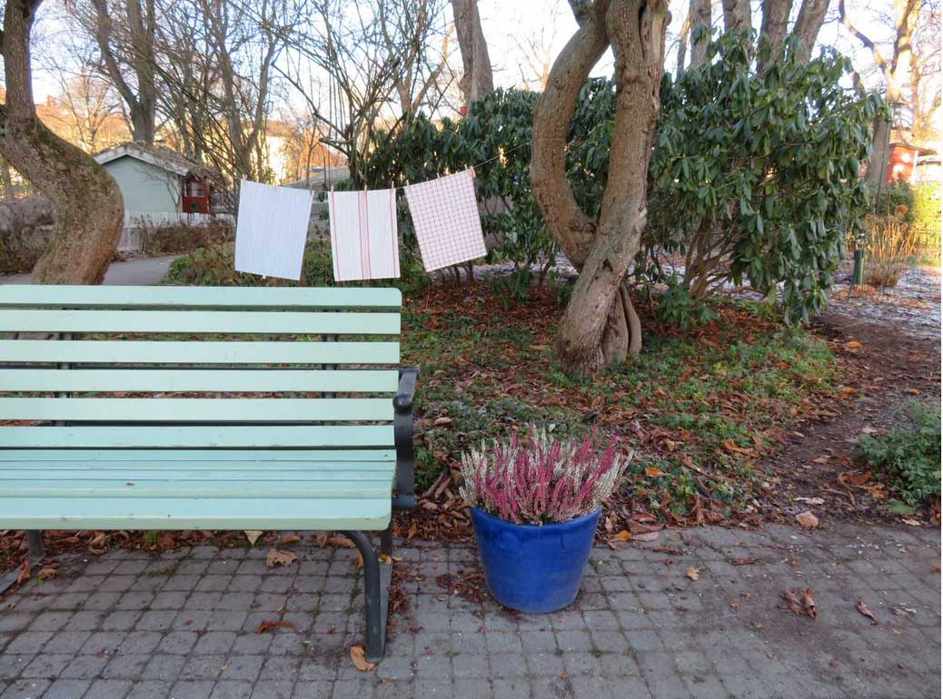 A photograph of a light green wooden bench in front of a washing line with white tea towels