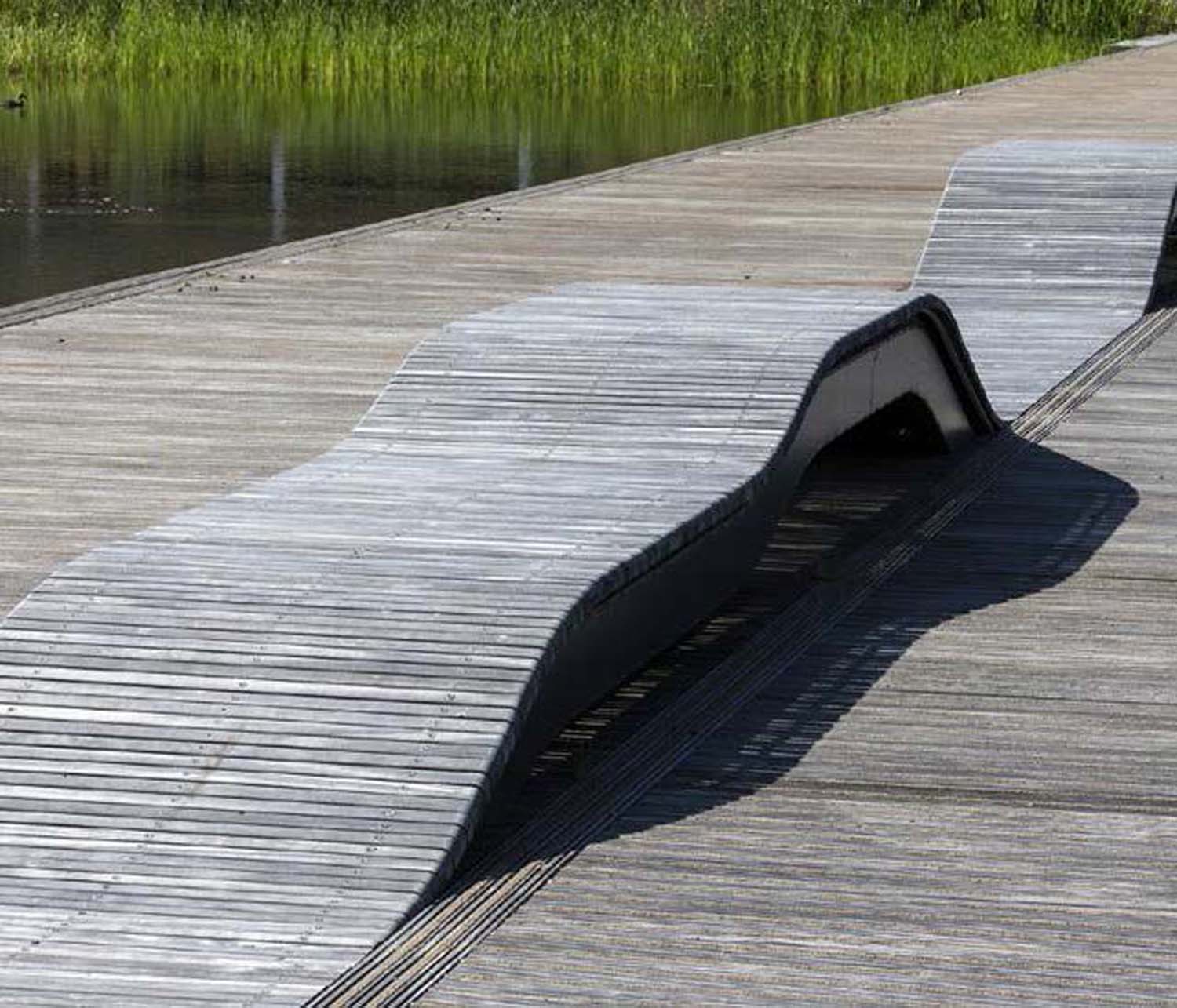 A photograph of a row of weathered wooden seating made from slats that rise in a wave form from the ground
