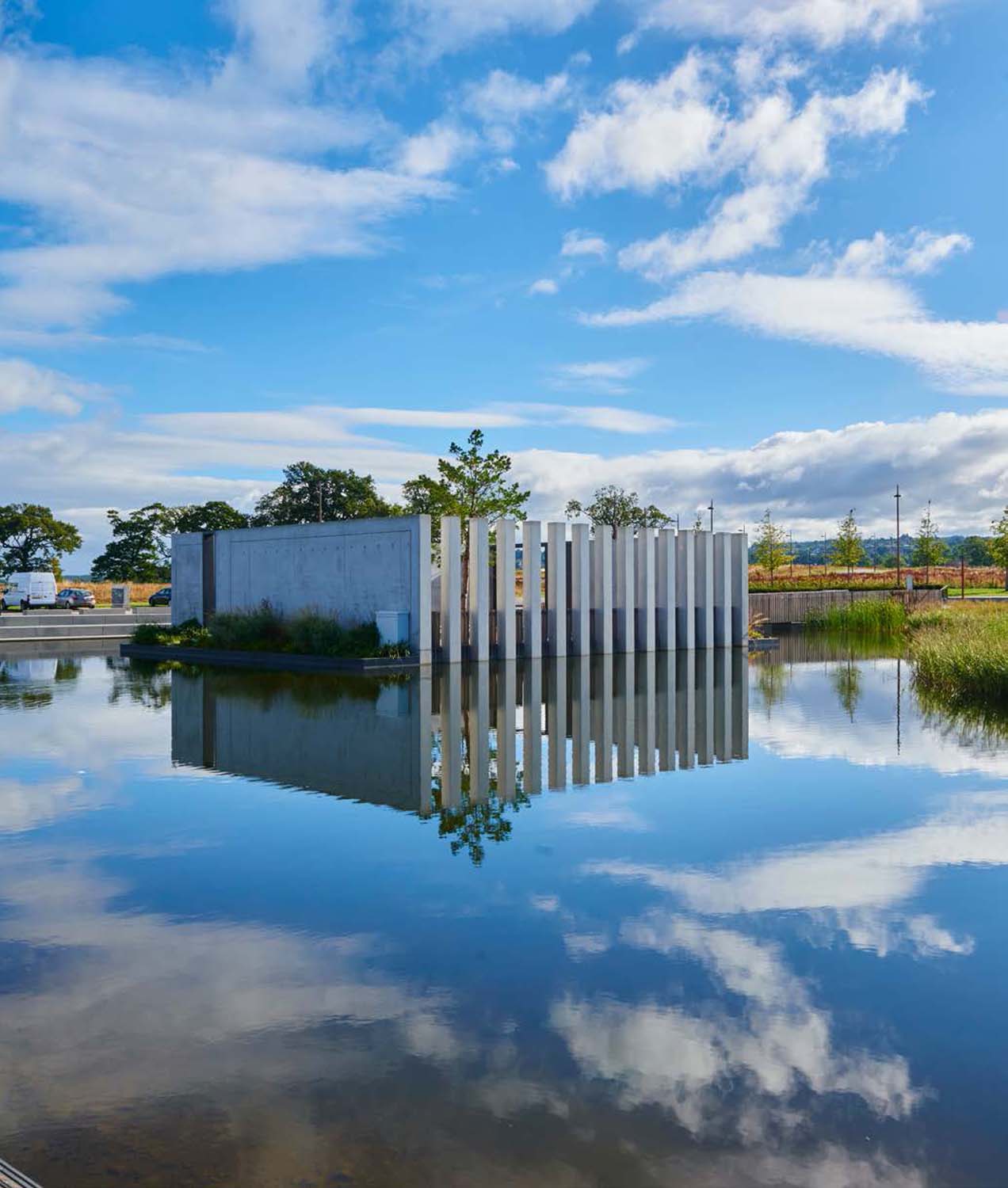A photo of a decorative structure of square concrete columns reflected in a still pond 