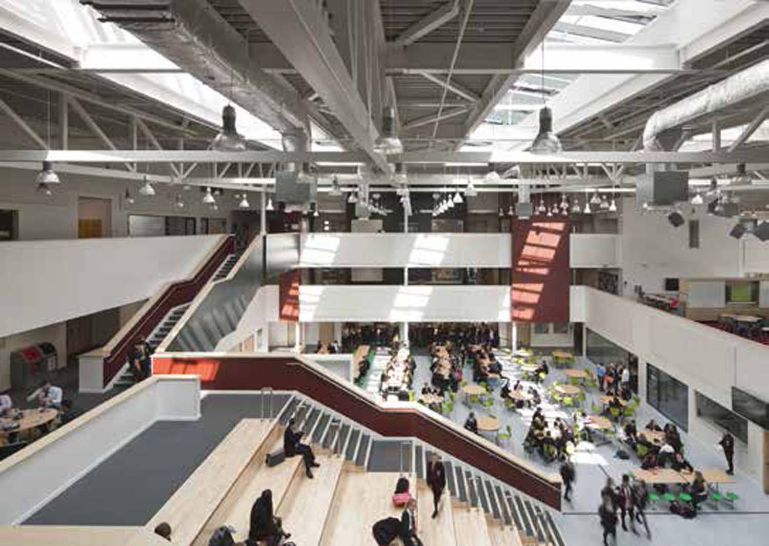 A two-storey atrium space filled with students. There are tables and amphitheatre sitting, and several spaces open up towards the atrium.