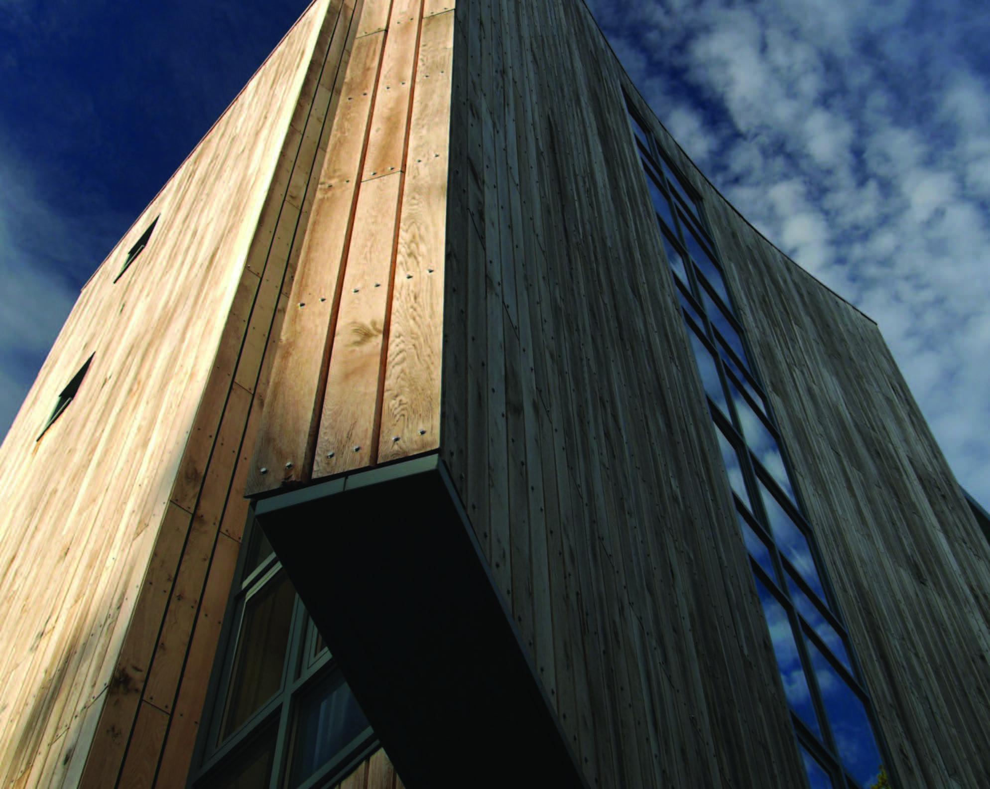 A close up of a corner of a timber-clad multi-storey building set against a blue sky