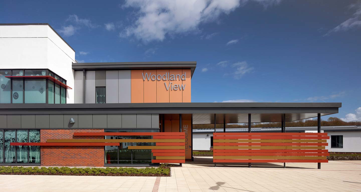 Woodland View's entrance on a sunny day, with large, metal cladding panels in bronze and silver-grey.