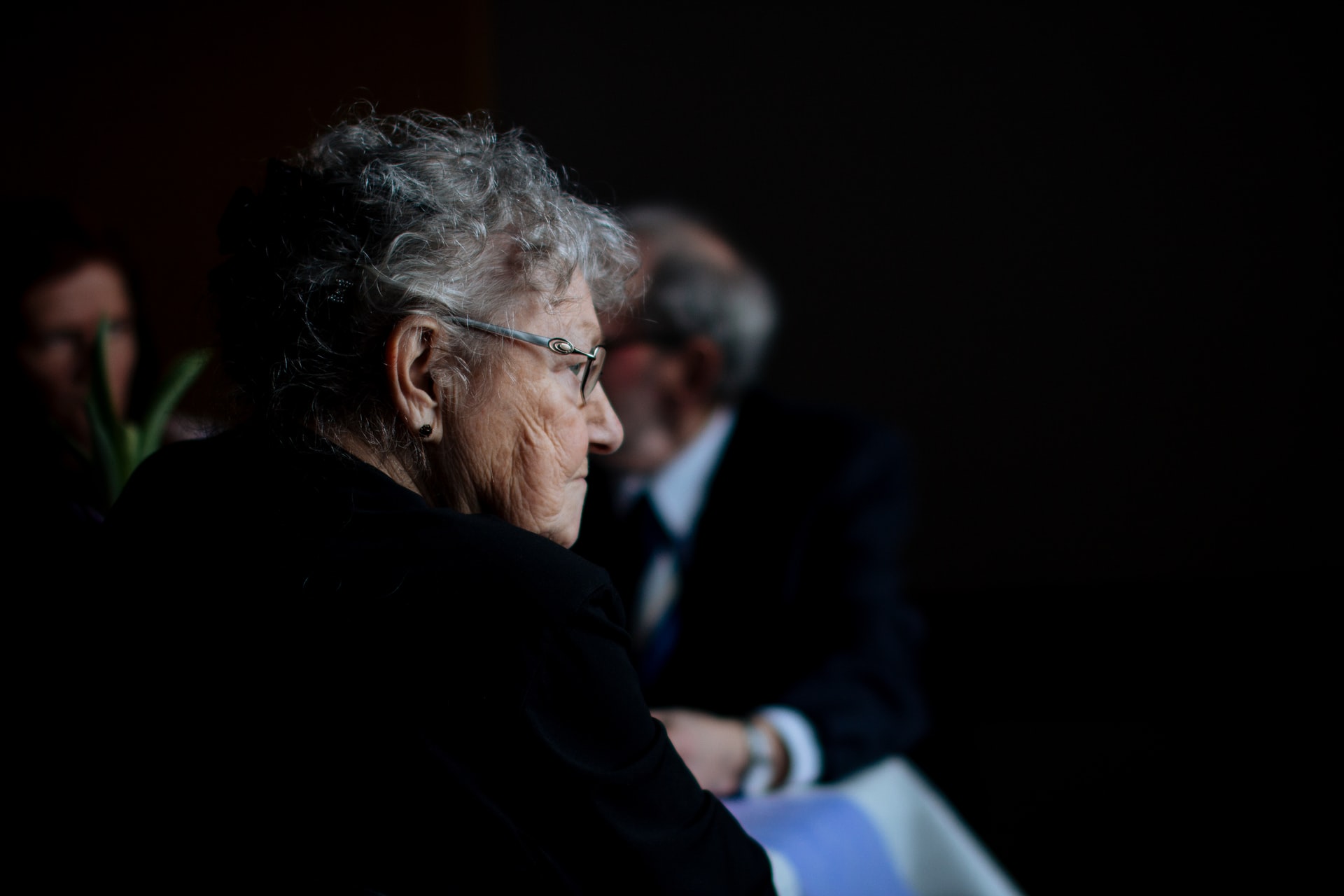 An elderly woman wearing glasses looks to the right.
