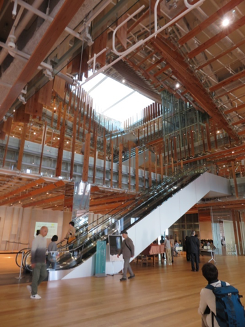 Light filters through a modern atrium in Toyama's Central Library and Museum. Prominent jagged wooden balustrade posts can be seen around the floors surrounding the atrium.