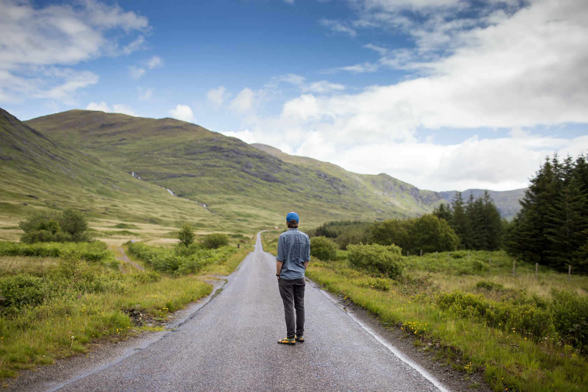 A man standing in the middle of a rural road on the Isle of Mull looking at hills in the distance.