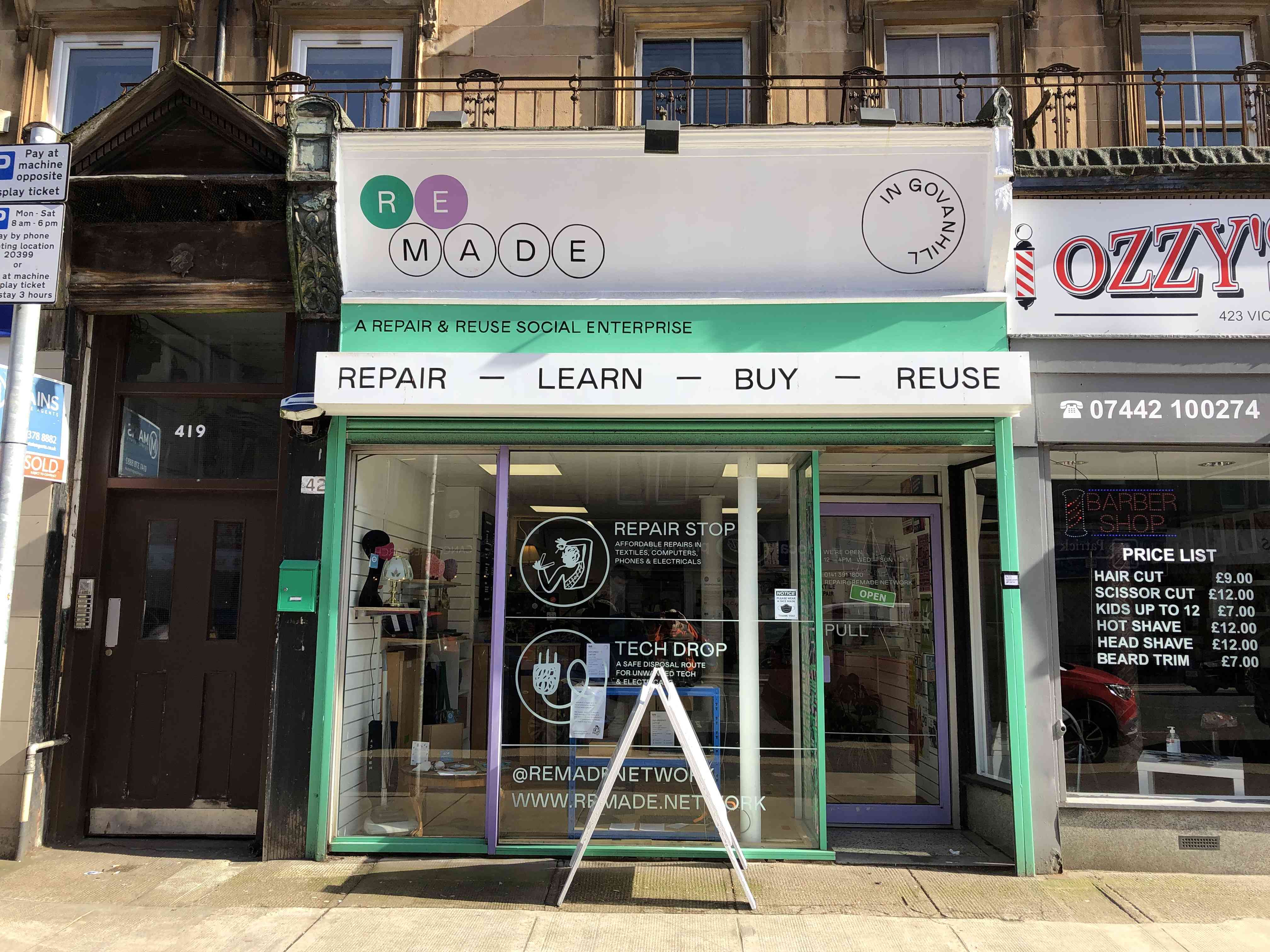 A street view of a green and white shop front with the following words: Remade in Govanhill; A repair and reuse social enterprise; repair, learn, buy, reuse; repair stop; tech drop. The shop is open.