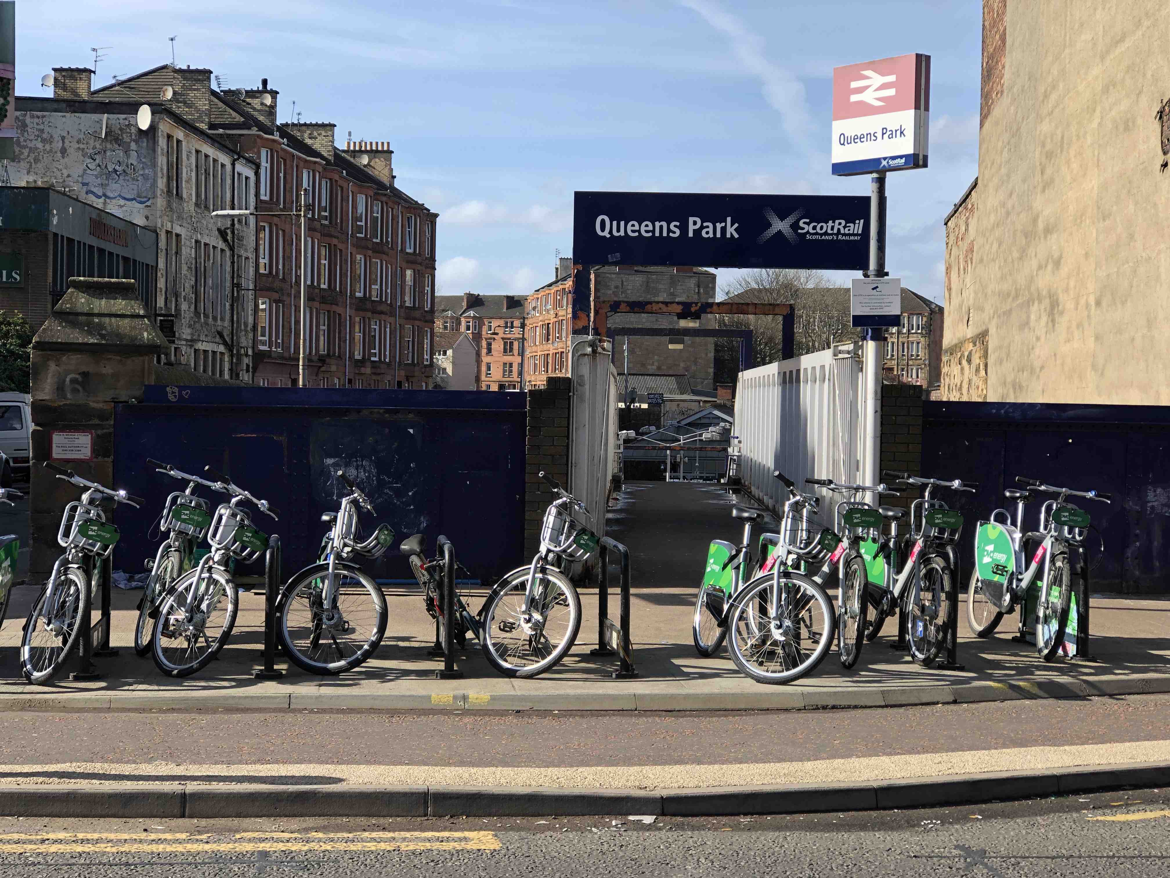 The entrance to Queens Park train station in Glasgow. About seven bicycles are parked in a row.