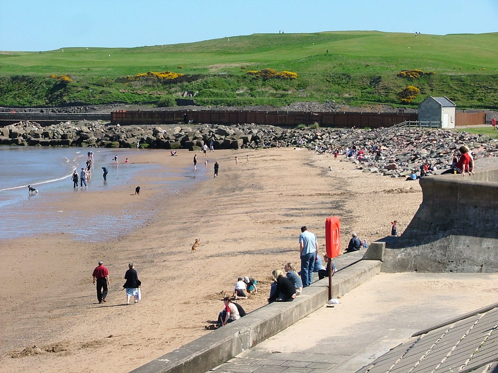 Locals in Aberdeenshire enjoy the beach on a sunny day. There are green hills in the distance.