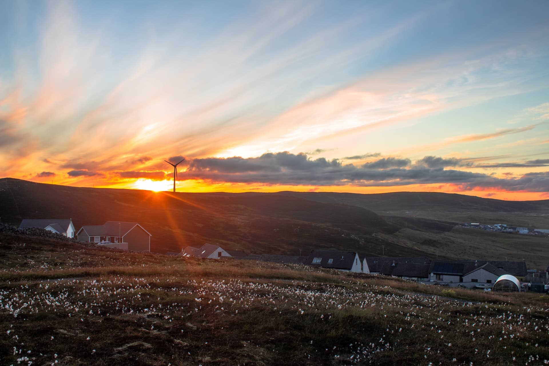 A housing settlement in Lerwick, Shetland, positioned in between hills during sunset. A single wind turbine is seen in the distance.