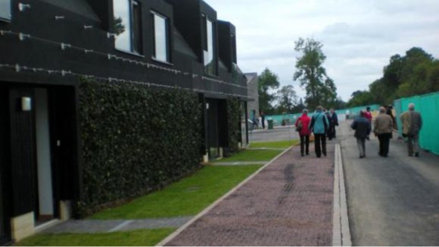 A dark bolding on the left hand side with a group of people standing on the pavement on the right