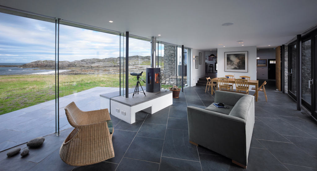 An open plan space  that contains the living area and a log burner over looks the rural and sea side landscape.