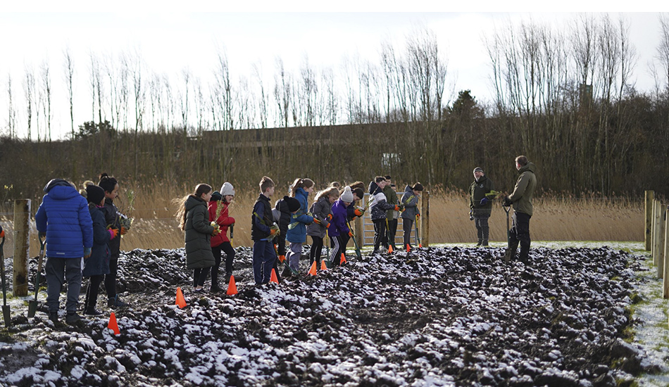 Pupils standing in a row as they plant trees for Queen Margaret University's Wee Forest.