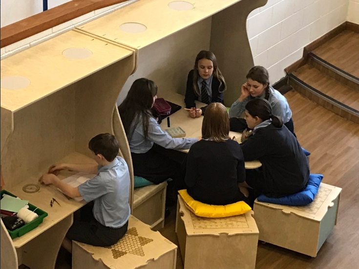 Children sitting together, talking and working in open space in school uniform.