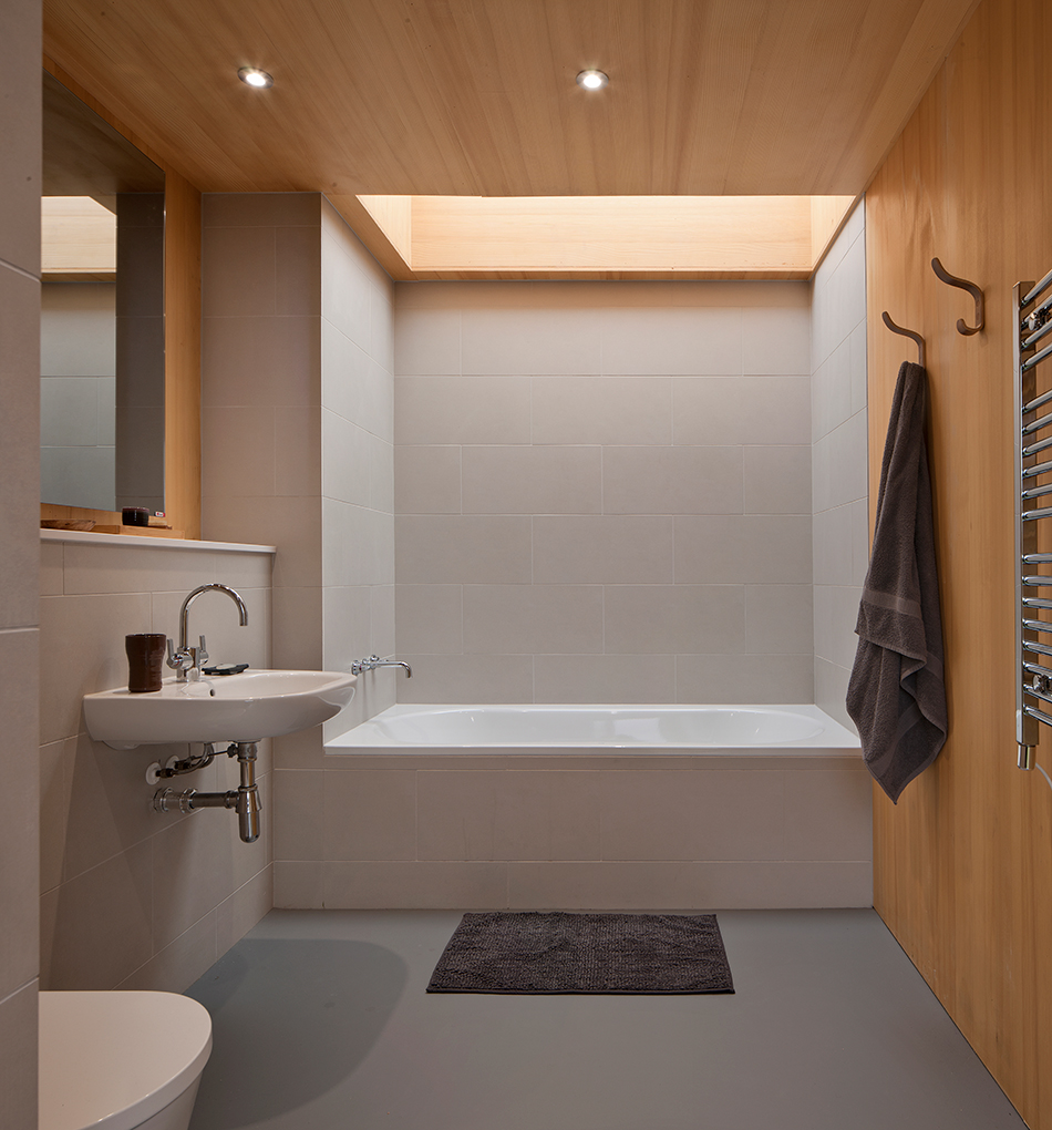 Bathroom at An Cala House features a sky light directly above the bath tub. Timber cladding surrounds the ceiling and wall in the space.