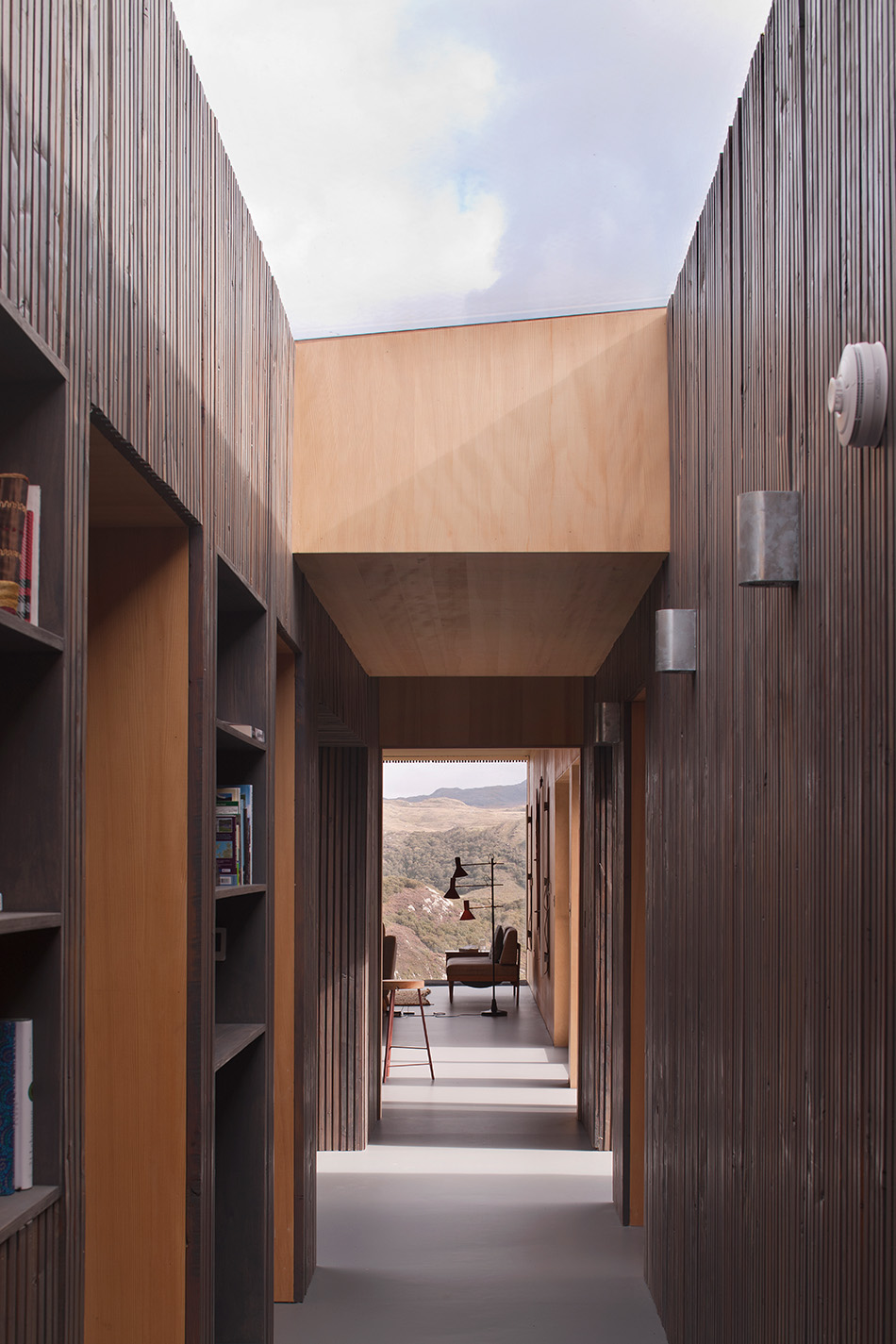 Corridor in An Cala House features a skylight. It connects all the rooms and the landscape is seen in the background through the floor to ceiling window in the living area.